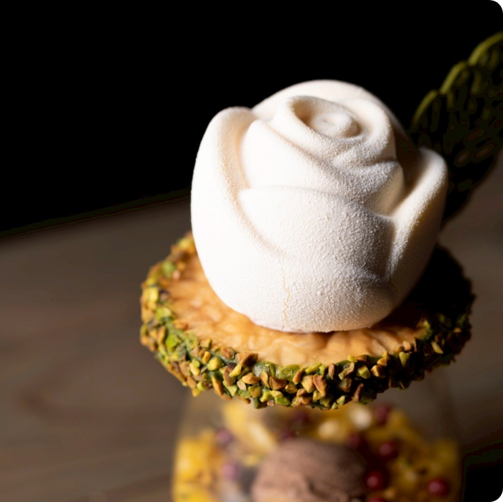 白いバラ型のムースが美しく飾られたパフェ。下にはナッツとフルーツが重なる芸術的な一品