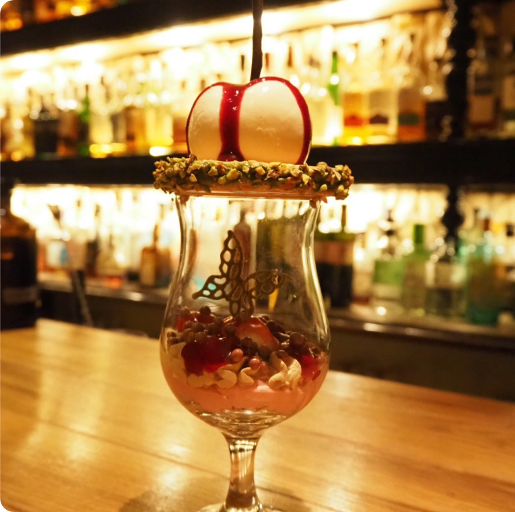 真っ赤なソースがかかった白い球体デザート。蝶のチョコ細工とナッツをあしらったグラスパフェ